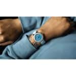 Stylish wristwatch with turquoise dial and metallic bracelet on cozy blue sweater.