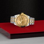 Elegant Tudor watch in gold and stainless steel against a luxurious black and red background.