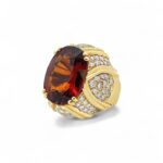 Elegant gold ring with a striking amber-orange gemstone and sparkling diamond accents.