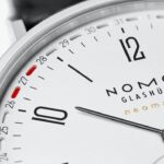 Elegant NOMOS Glashütte watch with minimalist design, silver-white dial, and red date indicator.