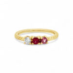 Elegant gold ring with twisted design and trio of colorful gemstones: diamond, ruby, and pink sapphire.