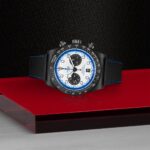 Stylish chronograph watch with black case, blue accents, and leather strap on a glossy surface.
