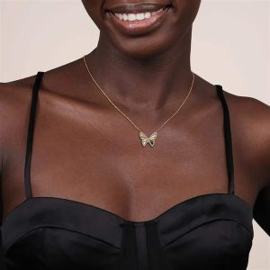 Woman smiling in a black top, showcasing an elegant butterfly necklace with gold accents.