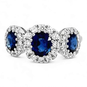 Elegant three-stone sapphire ring with diamond halo in polished white metal setting.