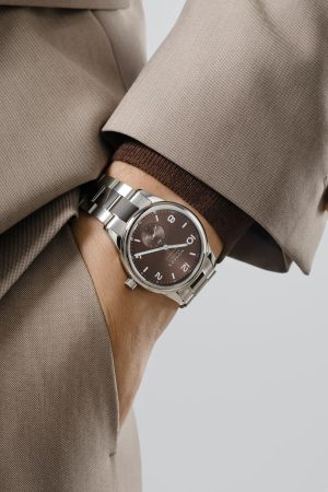 Stylish watch on wrist with brown dial, metallic case, and elegant suit jacket.