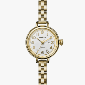 Elegant Shinola watch with gold-tone finish, white dial, and date window on metal bracelet.