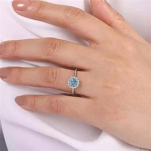 Elegant hand showcasing a striking blue gemstone ring on a soft neutral background.