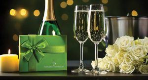 Champagne glasses, a gift box, candle, and roses create a perfect celebration atmosphere.
