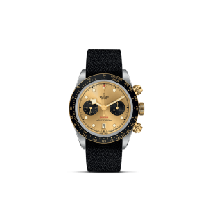 Tudor chronograph watch featuring a gold dial, black bezel, stainless steel case, and fabric strap.