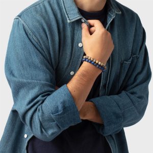 Casual denim shirt layered over navy with stylish bracelet on wrist against gray backdrop.