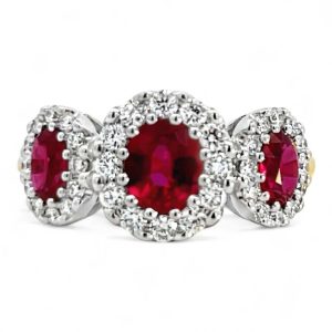 Elegant three-stone ruby ring with diamond halo, perfect for engagement or anniversary celebrations.